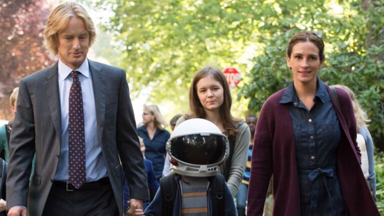 Cena do filme Extraordinário com o menino Auggie usando capacete de astronauta ao lado dos pais e da irmã na rua