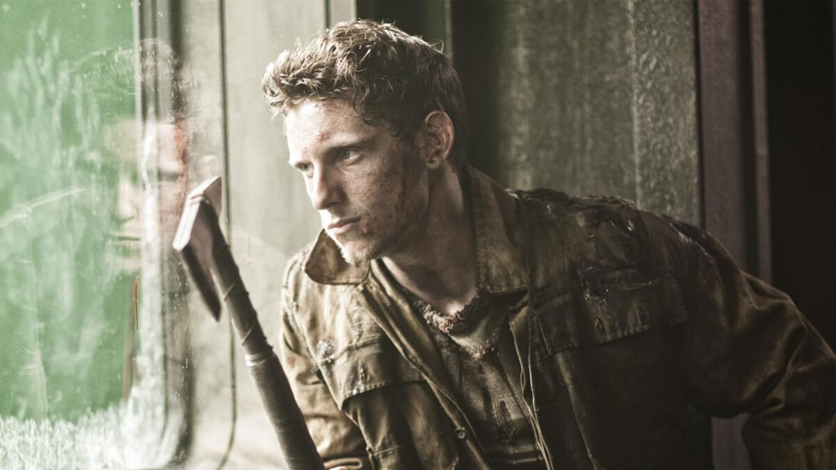 Jamie Bell com expressão séria e roupa suja segurando um machado dentro de um vagão no filme Expresso do Amanhã (2013)