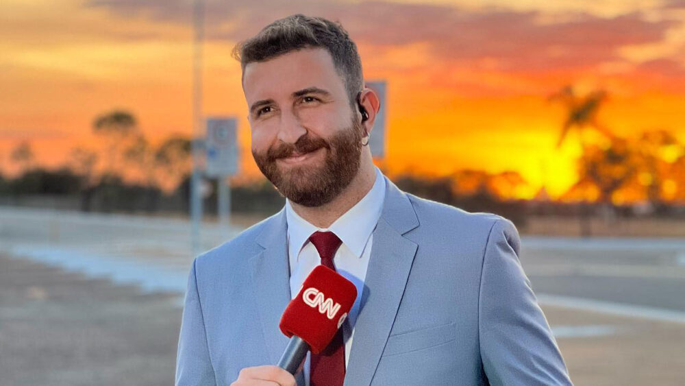 Teo Cury, novo analista da CNN Brasil, segura microfone da emissora durante trabalho em Brasília