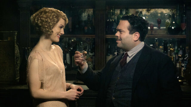 Alison Sudol e Dan Fogler em cena de Animais Fantásticos e Onde Habitam, brindando em um bar com garrafas ao fundo
