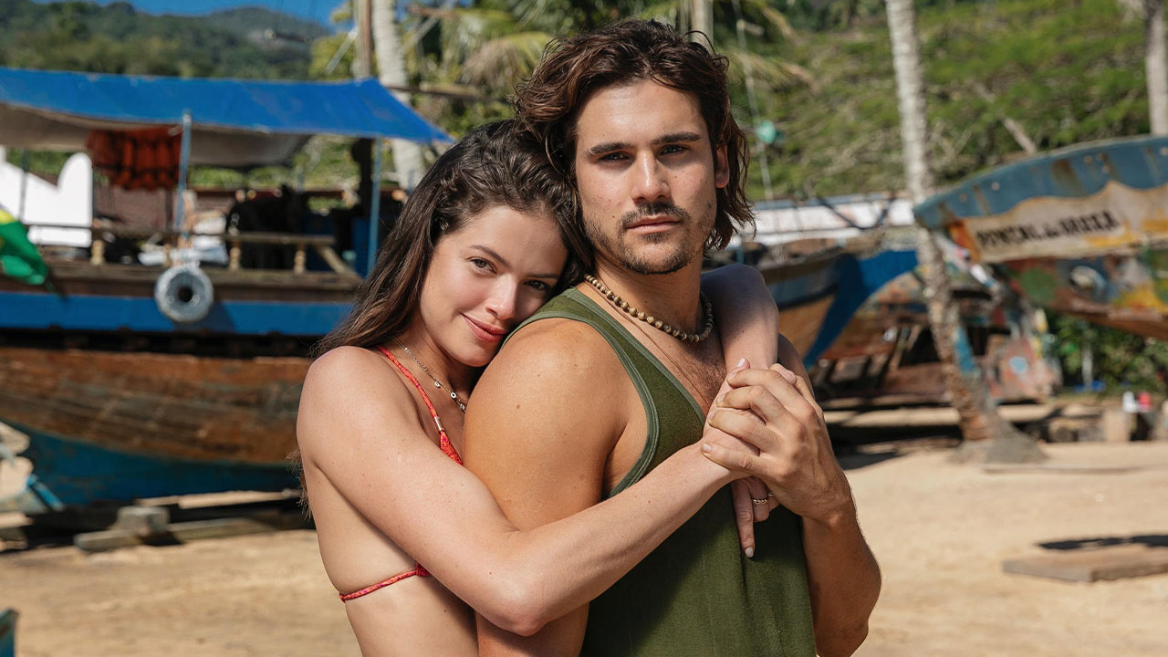 Luma (Agatha Moreira) e Rudá (Nicolas Prattes) abraçados em foto na praia na primeira fase de Mania de Você