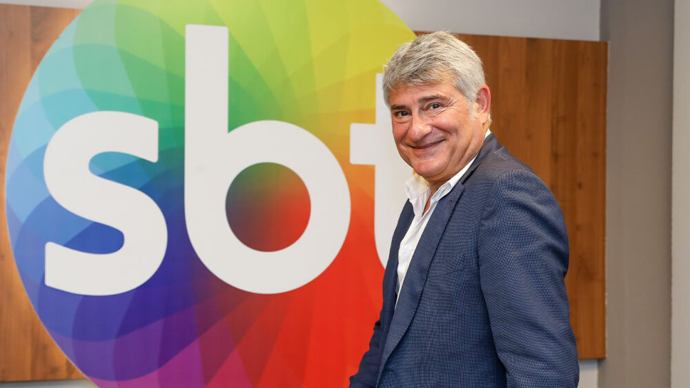 Cléber Machado com o logotipo do SBT ao fundo