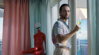 Mauricio Henao segura taça de espumante olhando pela janela em cena do filme Panamá