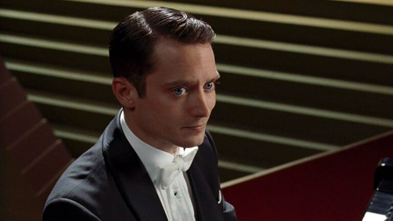 Elijah Wood com expressão séria vestindo smoking enquanto se prepara para tocar piano no filme Toque de Mestre (2013)