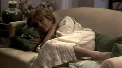 Maria Tereza (Glória Menezes) deitada no sofá com expressão de preocupação em cena da novela Corpo a Corpo