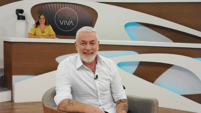 Alex Atala no centro do palco do Roda Viva com a apresentadora Vera Magalhães ao fundo