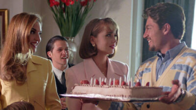 Cena da novela A Usurpadora com os personagens em uma festa segurando um bolo decorado com morangos e velas acesas