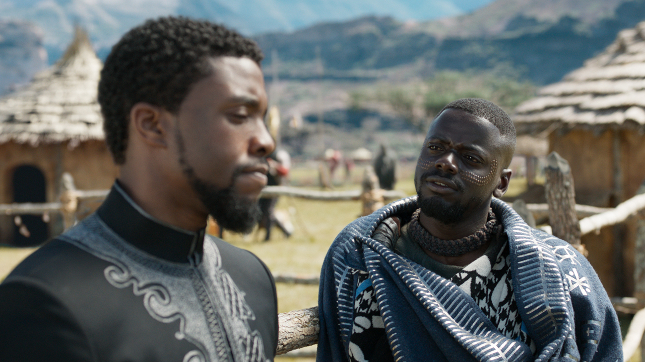 Chadwick Boseman e Daniel Kaluuya em cena de Pantera Negra (2018), com aldeia ao fundo