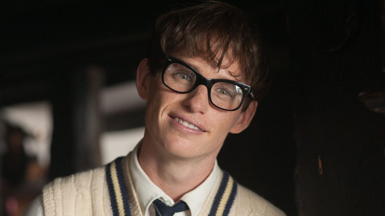 Eddie Redmayne como Stephen Hawking em cena de A Teoria de Tudo (2014), usando óculos e colete bege