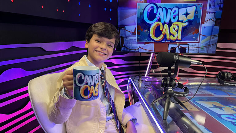Guilherme Tavares sentado em um estúdio de podcast, segurando uma caneca com a logo do CaveCast, sorrindo para a câmera