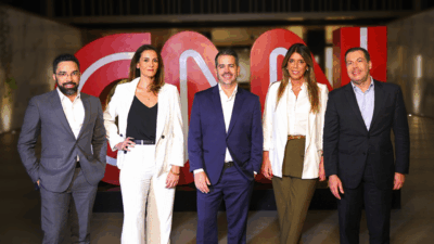 Henrique Simões, Mariana Garbin, Felipe Maia, Cris Vignoli e Fábio Ferri posam diante do logo da CNN Brasil em um ambiente corporativo