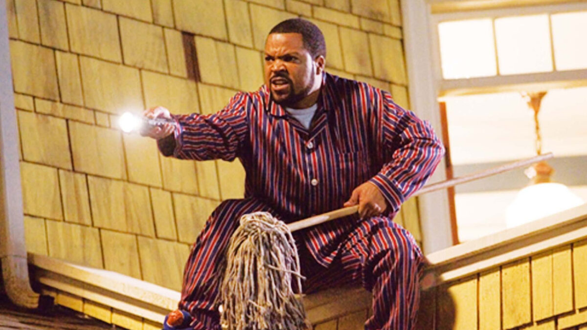 Ice Cube segurando uma vassoura e uma lanterna no telhado de uma casa em cena de Uma Casa de Pernas Pro Ar, que estará na programação de filmes da Band