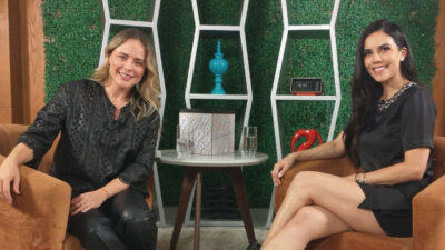 Juliana Silveira e Daniela Albuquerque sentadas em poltronas durante entrevista, sorrindo, com cenário decorado com prateleiras e plantas ao fundo