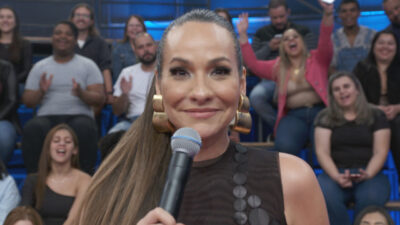 Maria Beltrão sorri enquanto segura um microfone no palco do programa Altas Horas, com a plateia animada ao fundo