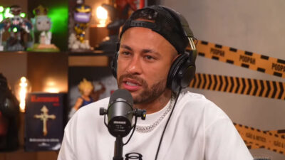 Neymar Jr. durante entrevista no podcast Podpah usando boné para trás, fones de ouvido e camiseta branca enquanto fala ao microfone