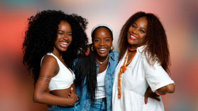 Nikolly Fernandes, Clara Moneke e Cyda Moreno sorrindo juntas, abraçadas, em foto de evento da novela Dona de Mim