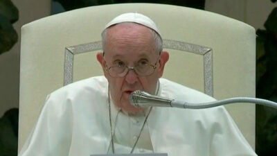 Papa Francisco fala ao microfone durante um evento oficial no Vaticano, usando vestes brancas e óculos