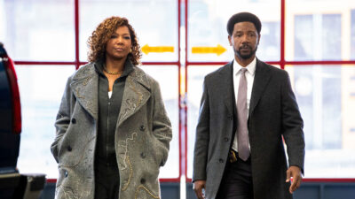 Queen Latifah e Tory Kittles em cena de The Equalizer. Eles estão de casaco cinza caminhando em um ambiente iluminado com janelas vermelhas