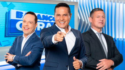 Thiago Gardinali, William Leite e Diógenes Lucca posam sorrindo no cenário do programa Balanço Geral, com fundo azul e branco