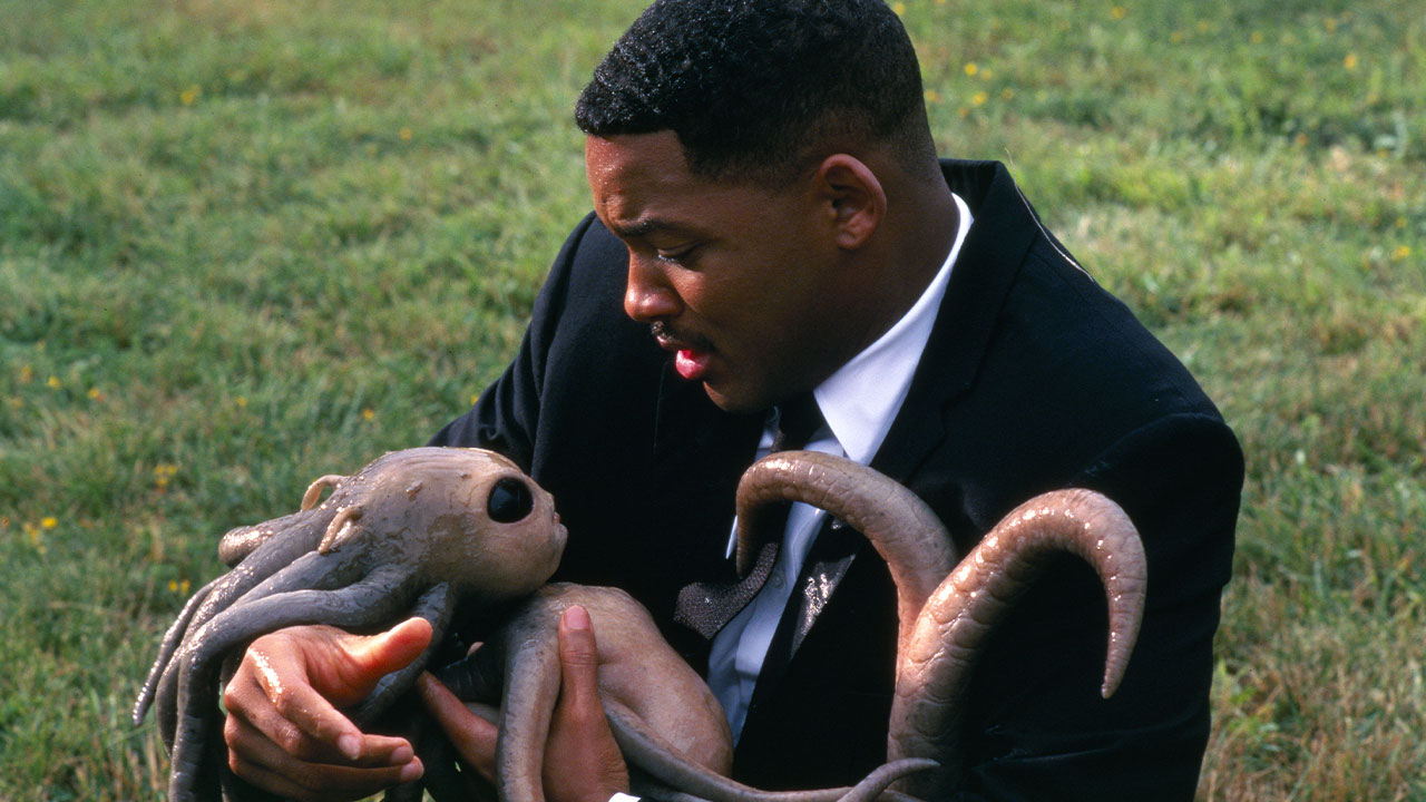 Will Smith em cena de MIB: Homens de Preto (1997), segurando um alienígena recém-nascido
