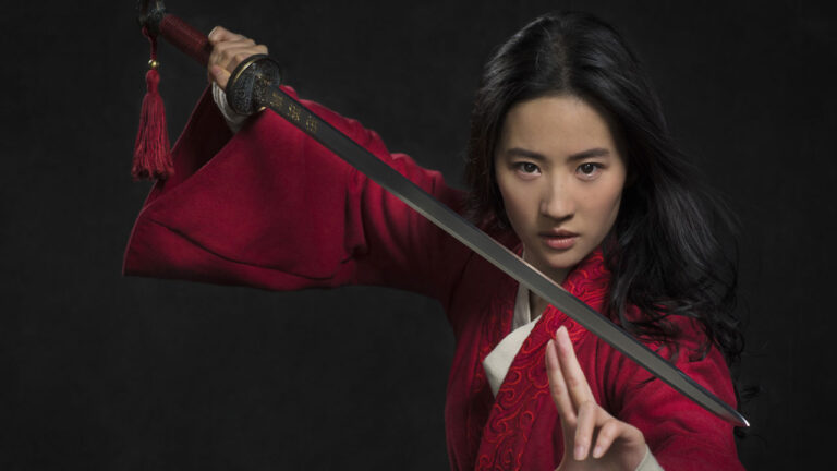 Yifei Liu em cena do filme Mulan, da TV Globo, vestindo traje vermelho e segurando uma espada em posição de combate