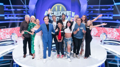 Tom Cavalcante e os participantes do programa Acerte ou Caia! posam sorridentes no palco, com o logotipo da atração ao fundo