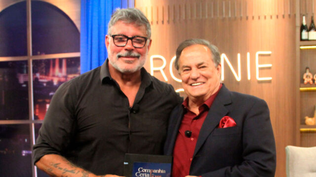 Alexandre Frota e Ronnie Von sorrindo no estúdio do programa Companhia Certa, com Frota segurando um livro