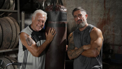 Antonio Fagundes e Marcos Mion no filme MMA - Meu Melhor Amigo, em um cenário rústico de academia, ao lado de um saco de pancadas