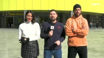 Carol Castro, André Linares e José Loreto em frente a um estádio, com André segurando um microfone da ESPN enquanto apresenta uma reportagem