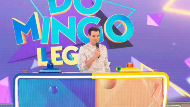Celso Portiolli apresenta o Passa ou Repassa no palco do Domingo Legal com bancada colorida e microfone na mão