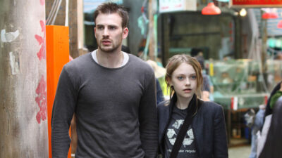 Chris Evans e Dakota Fanning em cena do filme Heróis (2009) andando por uma rua movimentada