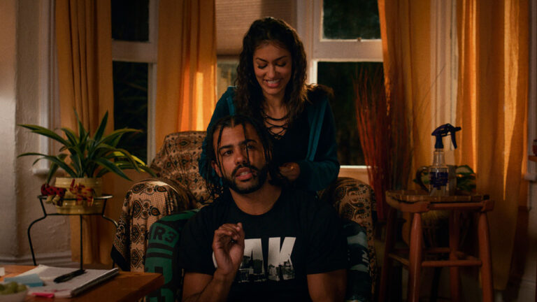 Daveed Diggs sentado enquanto Janina Gavankar arruma seu cabelo em cena do filme Ponto Cego de 2018