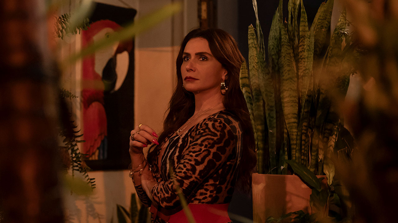 Giovanna Antonelli como Elvira na novela Beleza Fatal, em cena com expressão séria, rodeada por plantas em ambiente intimista