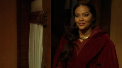 Esther De Oliveira caracterizada como Ariana na série Neemias, vestindo manto vermelho e sorrindo em um ambiente com iluminação quente