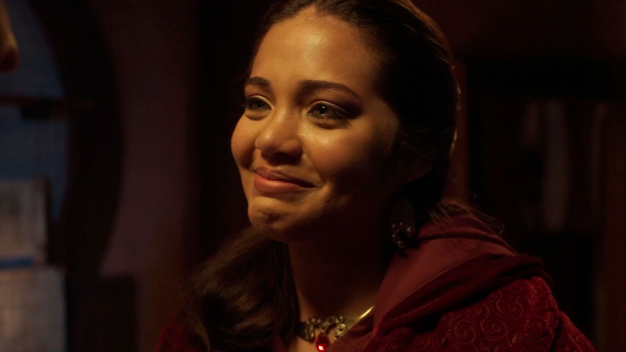Esther De Oliveira como Ariana na série Neemias, emocionada e com lágrimas nos olhos, vestindo manto vermelho em cena com luz baixa