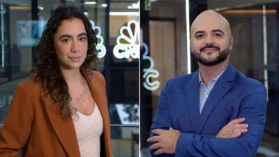 Giulia Pradal e Miguel Brito posam em frente ao logotipo da CNBC, usando trajes sociais.