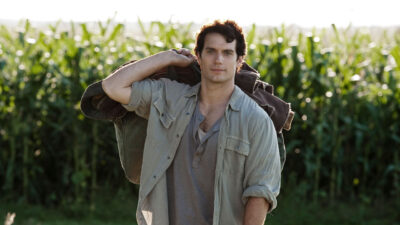 Henry Cavill caracterizado como Clark Kent em cena de Homem de Aço diante de plantação de milho