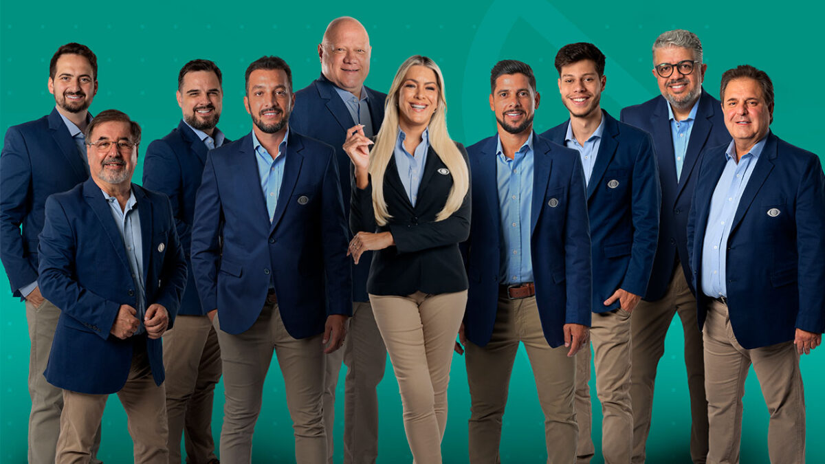 Renata Fan ao centro com os nove comentaristas do Jogo Aberto usando blazer azul e calça bege em fundo verde