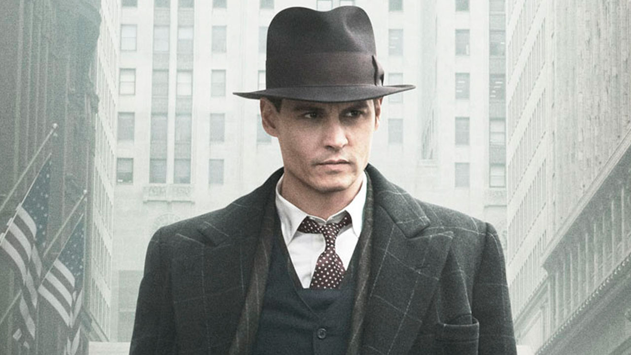 Johnny Depp caracterizado como John Dillinger, usando terno e chapéu, caminhando em uma rua com prédios altos ao fundo no filme Inimigos Públicos (2009)