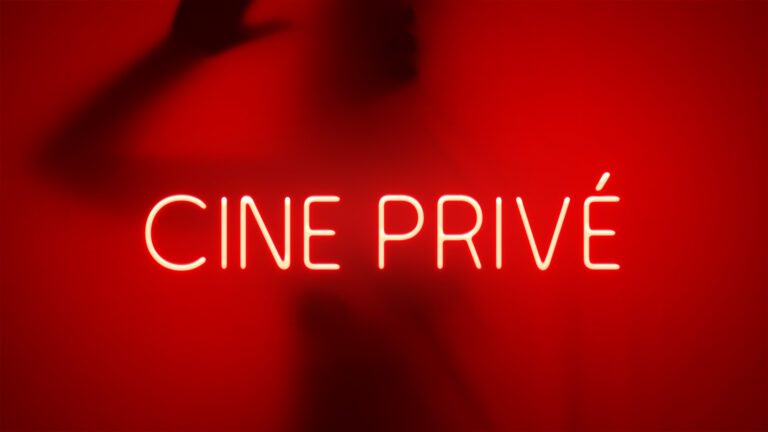 Letreiro em neon com o nome Cine Privé em fundo vermelho com silhueta desfocada ao fundo