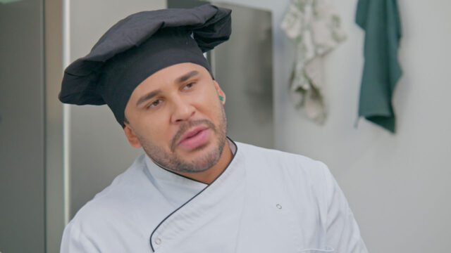 Lucas Guimarães vestido de chef de cozinha no programa Eita Lucas! do SBT, em uma cozinha profissional com panos pendurados ao fundo