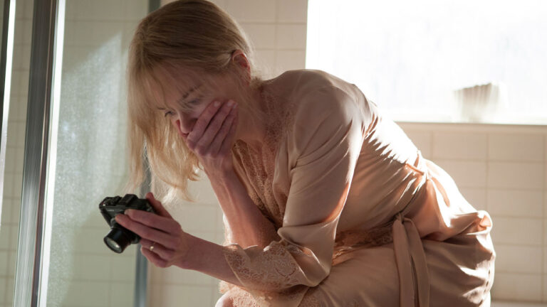 Nicole Kidman caracterizada como Christine em Antes de Dormir (2014), usando robe de cetim, segurando uma câmera e cobrindo a boca com expressão de choque em um banheiro iluminado