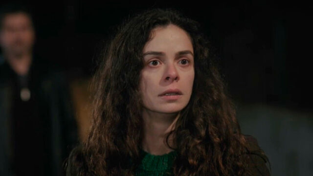 Atriz Özge Özpirinçci como Bahar em cena tensa de Força de Mulher, com expressão assustada e olhos marejados, usando suéter verde, enquanto um homem desfocado aparece ao fundo