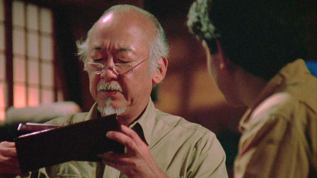 Pat Morita, no papel do Sr. Miyagi, segura uma carteira enquanto conversa com Ralph Macchio, que interpreta Daniel LaRusso, em uma cena do filme Karatê Kid III - O Desafio Final (1989)
