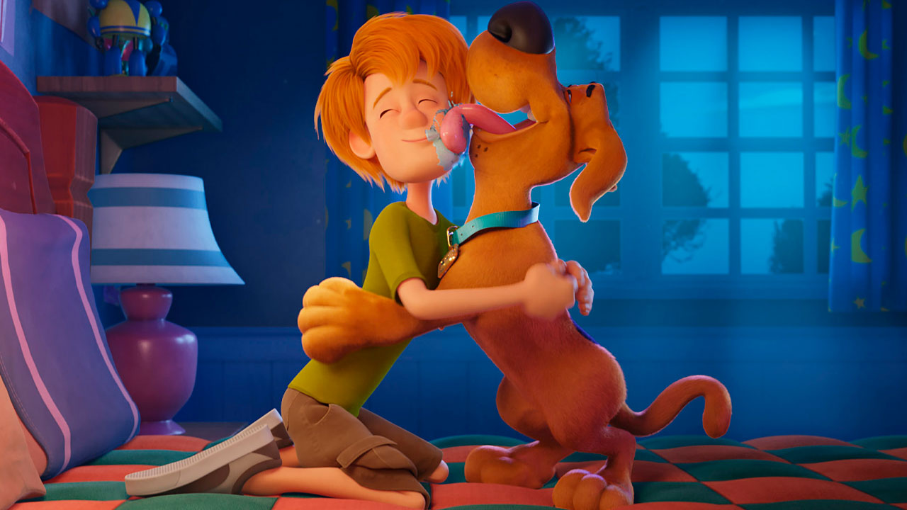 Cena da animação Scooby! O Filme com Salsicha abraçando Scooby-Doo, que o lambe no rosto, em um quarto iluminado pela luz azul da noite