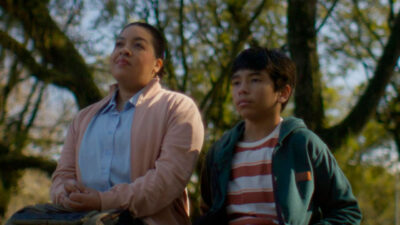 Silvana Rodrigues e João Marcelo Dalla Ros observam o horizonte sentados em um banco sob árvores em um ambiente natural no filme Família Em Construção (2025)