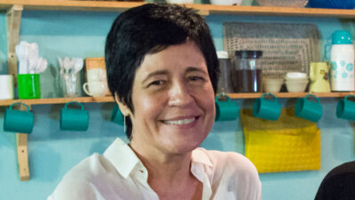 Thelma Guedes sorrindo com uma prateleira com utensílios domésticos eo fundo