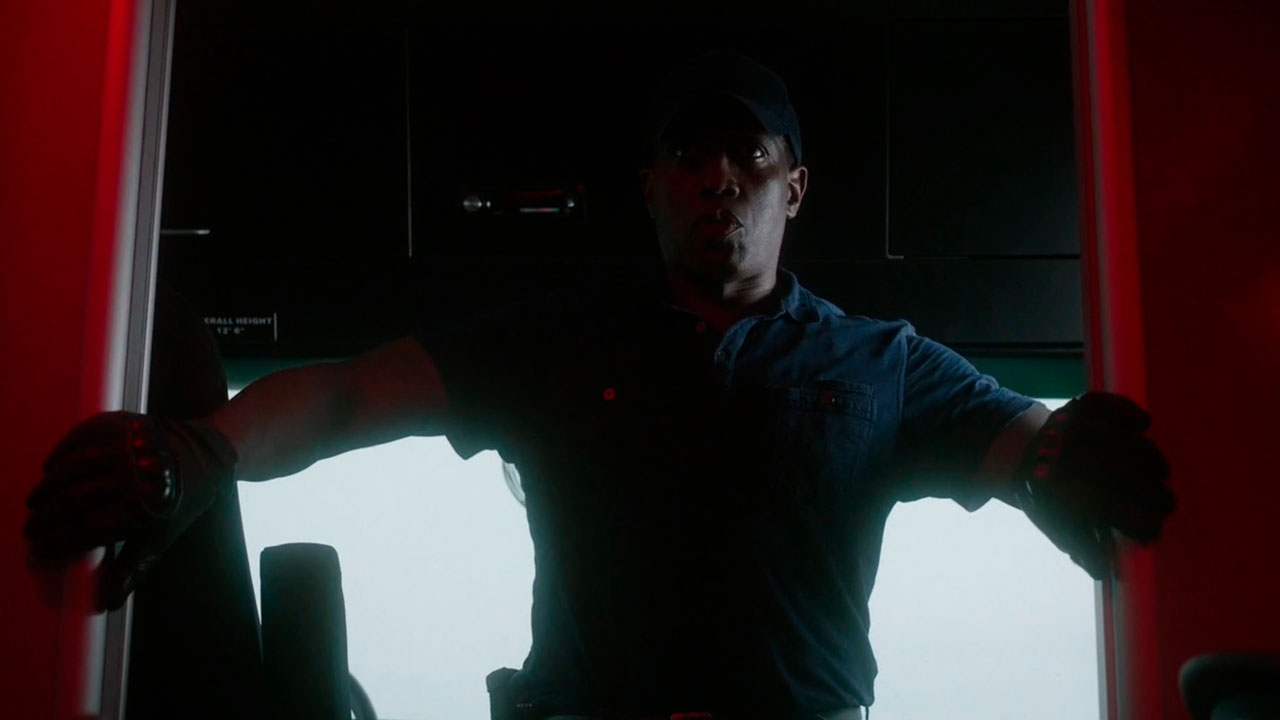 Wesley Snipes caracterizado como Isaac em Resposta Armada (2017), usando boné e luvas enquanto abre uma porta em um ambiente escuro com iluminação vermelha