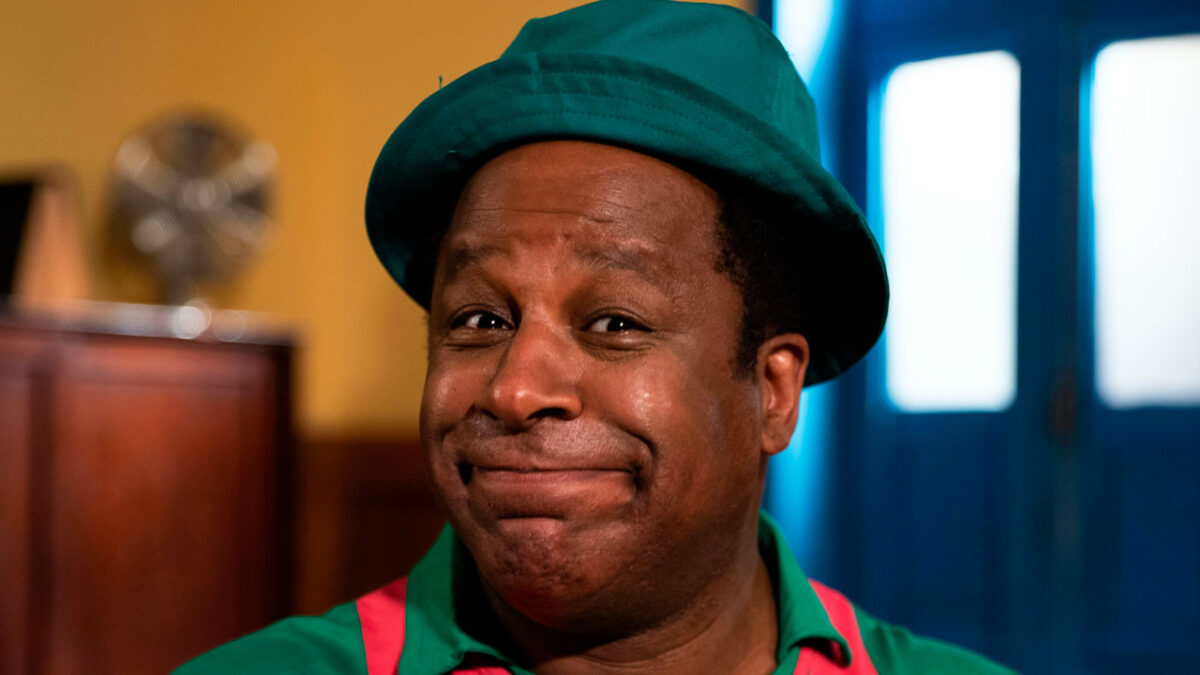 Ailton Graça caracterizado como Mussum com expressão divertida em cena de filme biográfico