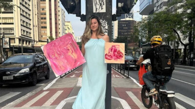 Bella Mantovani em ciclovia da Avenida Paulista segurando duas telas de pintura abstrata em tons de rosa